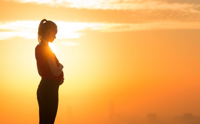 Pregnant woman standing alone holding her belly during sunset. Maternity and motherhood care.