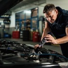 Auto mechanic using lap while examining car engine in repair sho