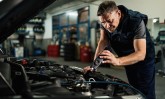 Auto mechanic using lap while examining car engine in repair sho