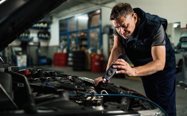 Auto mechanic using lap while examining car engine in repair sho