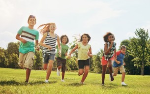 Happy kids, playing and running with grass field in nature for fun, playful day or sunshine at park. Diversity or group of excited children or youth enjoying sunny outdoor holiday or weekend together
