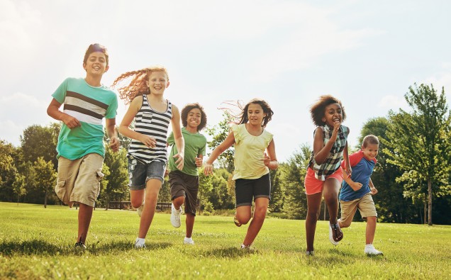 Happy kids, playing and running with grass field in nature for fun, playful day or sunshine at park. Diversity or group of excited children or youth enjoying sunny outdoor holiday or weekend together