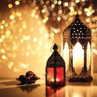 Ornamental Arabic lanterns with burning candles. Glittering golden bokeh lights. Plate with date fruit on the table. Greeting card for Muslim holiday Ramadan Kareem. Iftar dinner background.