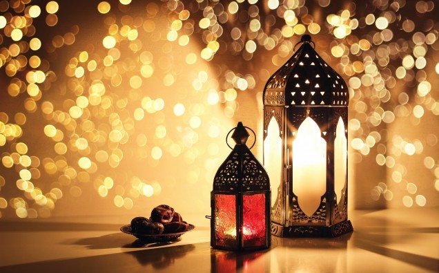 Ornamental Arabic lanterns with burning candles. Glittering golden bokeh lights. Plate with date fruit on the table. Greeting card for Muslim holiday Ramadan Kareem. Iftar dinner background.